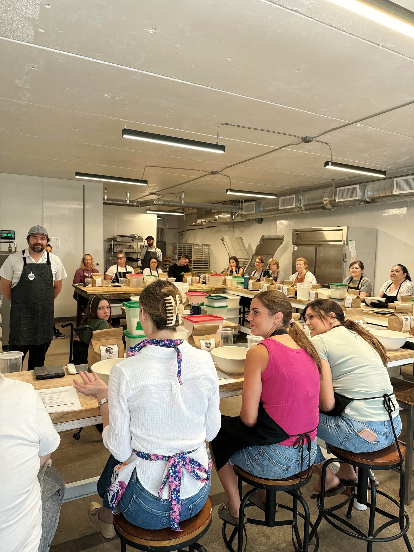 Group of people in a kitchen setting, possibly a cooking class or workshop.